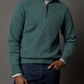 A person wears a Sid Mashburn Half-Zip Sweater in green over a plaid shirt with dark blue jeans, standing against a plain gray background.