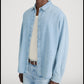 A person wearing the Frame Classic Denim Shirt—a relaxed fit, 100% cotton denim shirt—over a cream knit tank top, paired with light blue jeans and a brown belt.