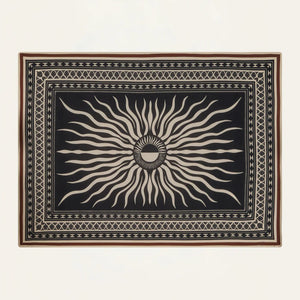The Golden Horizon Pareo by Johanna Ortiz features a black background with a central beige sunburst and geometric borders—an eye-catching accessory to elevate your style, as versatile and striking as a chic scarf or wrap.