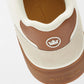 Close-up of the heel of the Peter Millar Drift Mesh Sneaker in brown and beige, featuring a crown logo, "Peter Millar" branding on the sole, and herringbone traction for grip.