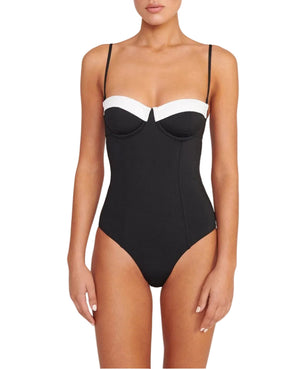 A woman wearing the Maeve One Piece by Staud, a black swimsuit featuring thin removable straps and a contrasting white band across the top.