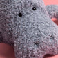 Close-up of the gray, textured Jellycat Maffles Manatee plush with black button eyes on a pink background—ideal for anyone who adores whimsical sea creatures.