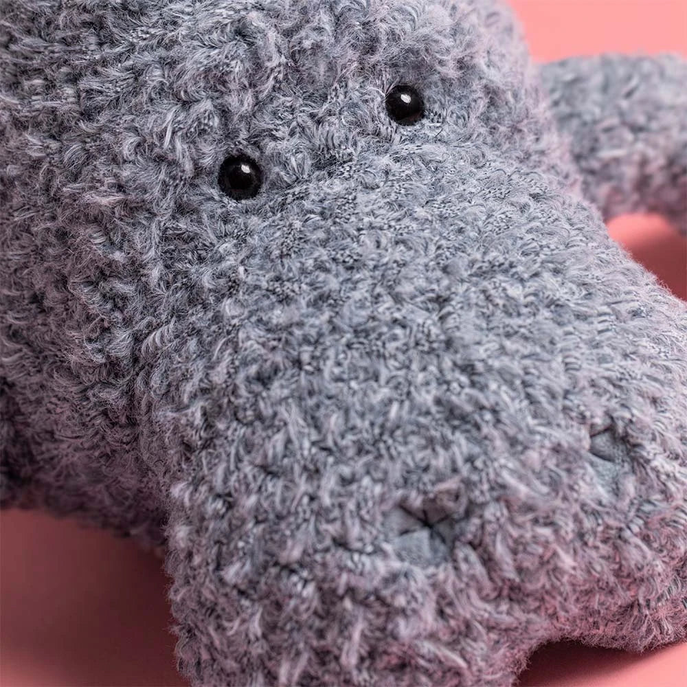 Close-up of the gray, textured Jellycat Maffles Manatee plush with black button eyes on a pink background—ideal for anyone who adores whimsical sea creatures.