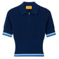 The Marcella Polo by Guest in Residence is a short-sleeve navy blue knit top in soft pique stitch with a zippered collar, ribbed waist, and light blue and white stripes on the sleeves and hem.