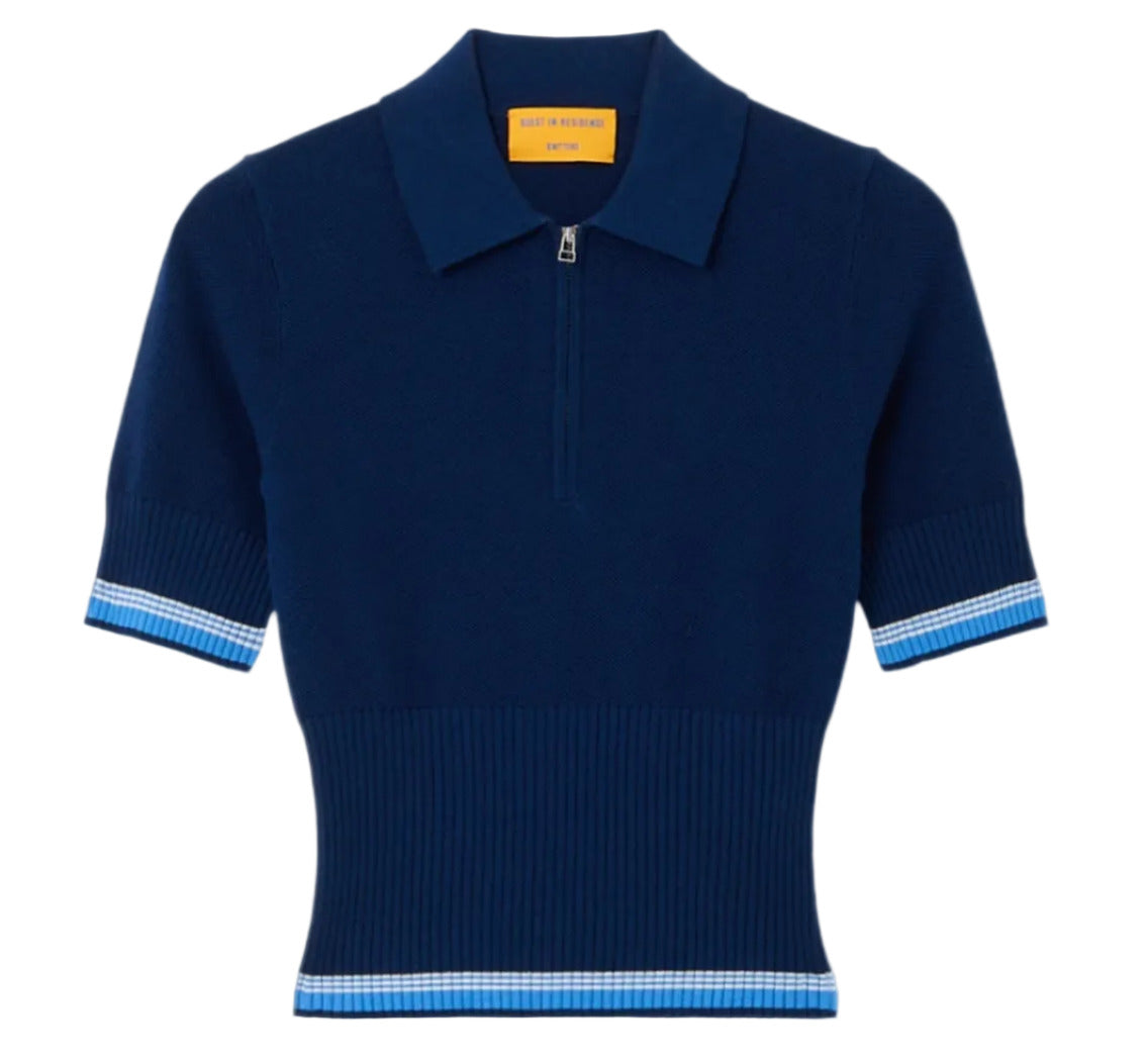 The Marcella Polo by Guest in Residence is a short-sleeve navy blue knit top in soft pique stitch with a zippered collar, ribbed waist, and light blue and white stripes on the sleeves and hem.