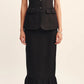 A woman wears the POSSE Matilda Column Skirt—a high-rise, ruffled-hem piece—paired with a sleeveless, button-up black vest with ruffle pockets and black flats.