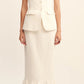 A woman wears a sleeveless, buttoned ivory vest with peplum detail and the POSSE Matilda Column Skirt in premium linen, featuring a high-rise waist and ruffled hem, paired with black flats.