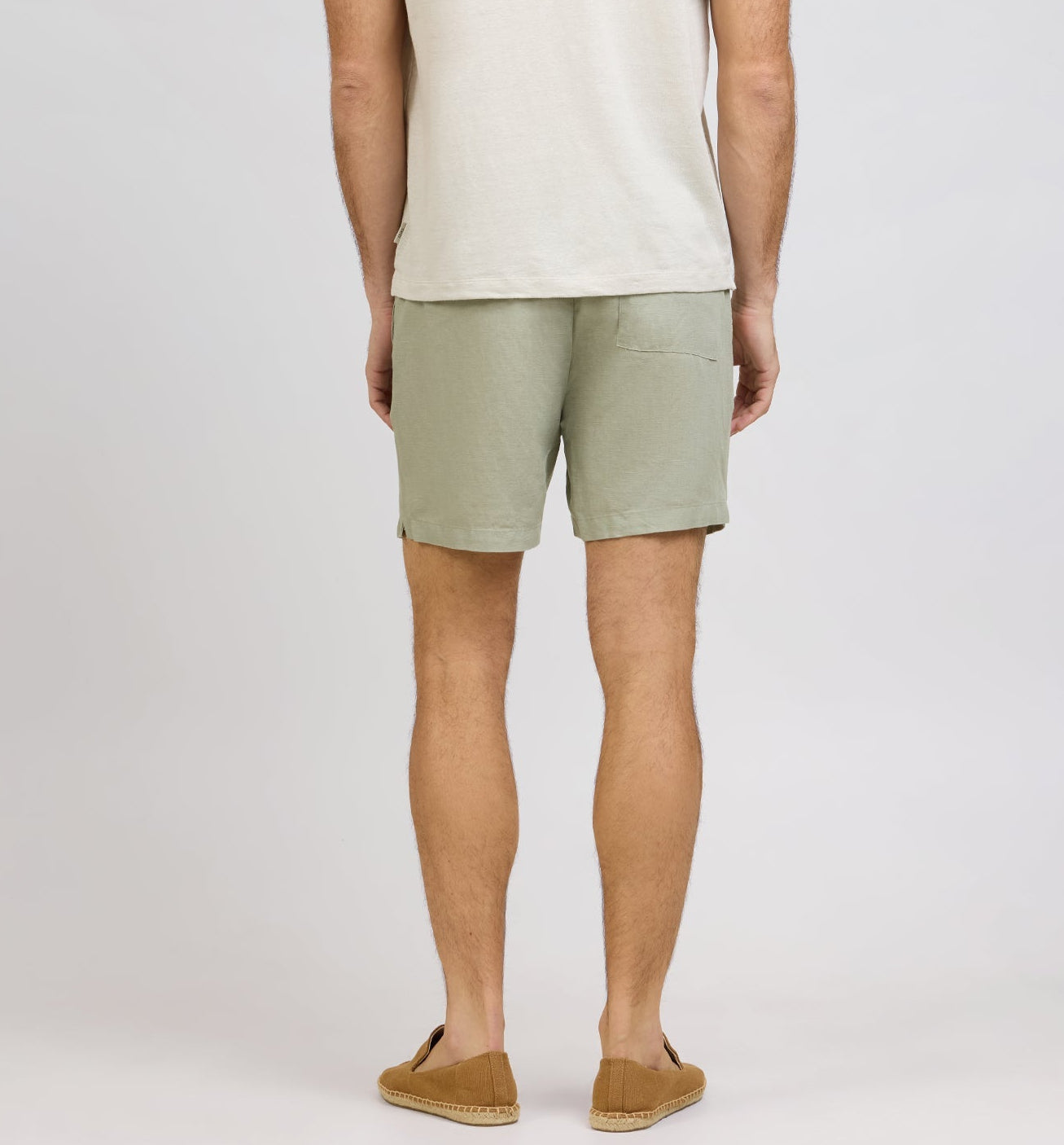 A person is shown from the back against a plain background, wearing a light beige t-shirt, Onia Air Linen Pull-On Short with a stretch waist and back pocket, and tan espadrille shoes.