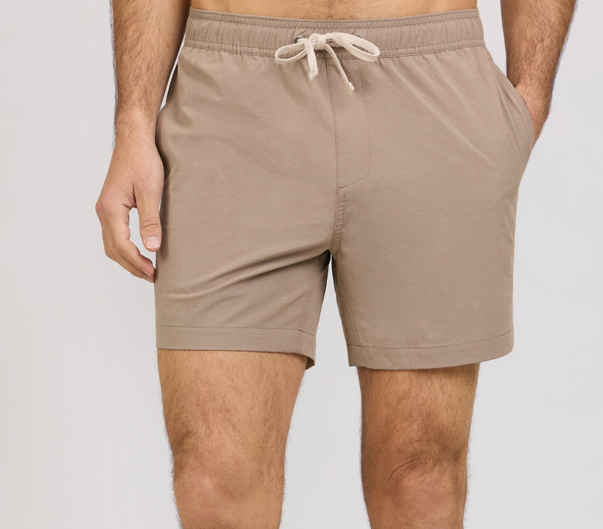 A person wearing light brown Onia Land to Water Short 6" with four-way stretch, hands in pockets, shown from mid-torso to mid-thigh against a plain background.