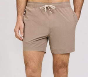 A person wearing light brown Onia Land to Water Short 6" with four-way stretch, hands in pockets, shown from mid-torso to mid-thigh against a plain background.