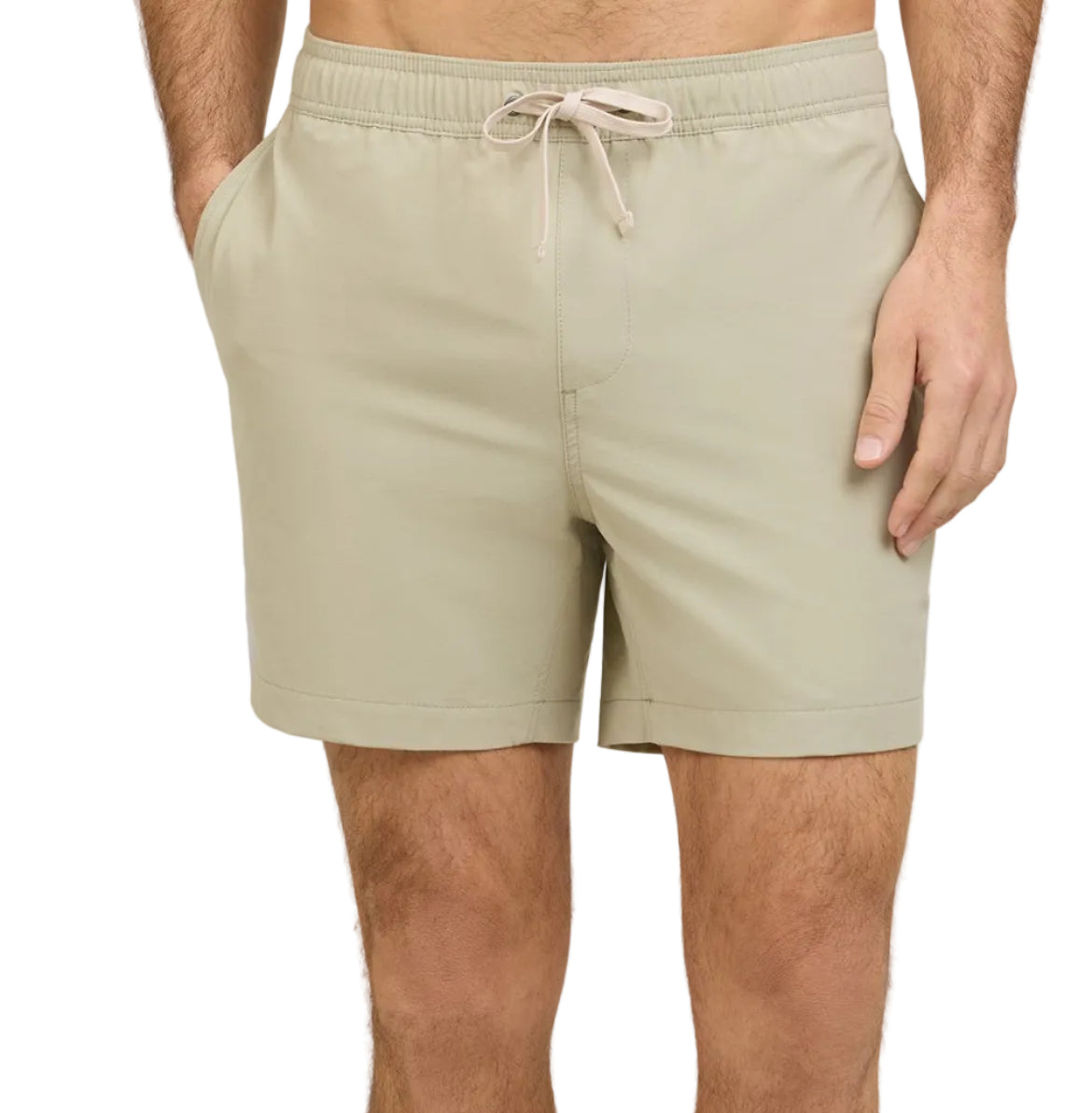 A person wearing Onia Land to Water Short 6" in light beige, featuring a drawstring waistband and side pockets, stands with one hand in a pocket.