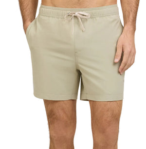 A person wearing Onia Land to Water Short 6" in light beige, featuring a drawstring waistband and side pockets, stands with one hand in a pocket.