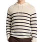 A person wearing the Onia Frank Hooded Sweater, a long-sleeve cream linen hoodie with black stripes and drawstrings, paired with brown pants.