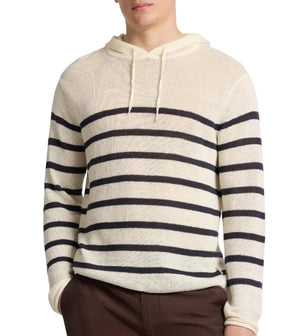 A person wearing the Onia Frank Hooded Sweater, a long-sleeve cream linen hoodie with black stripes and drawstrings, paired with brown pants.