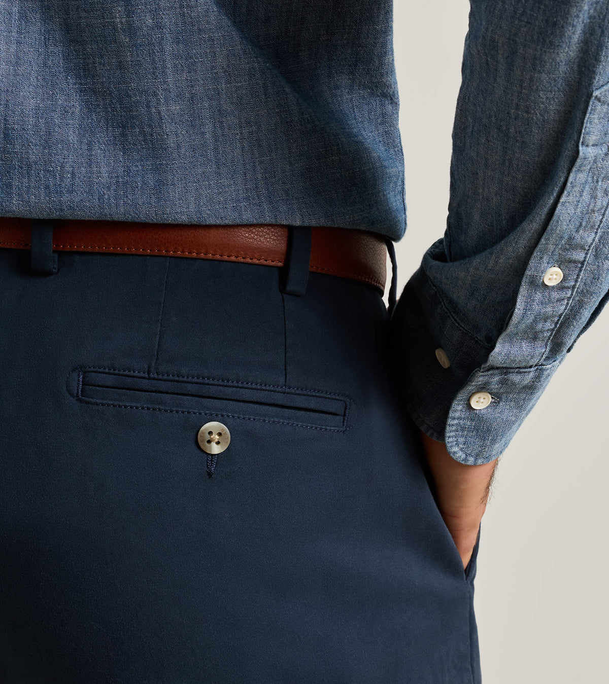 Navy Peter Millar Signature Sateen Flat Front Trouser in stretch cotton with a single button-closure back pocket and a brown leather belt, worn with a blue button-down shirt.