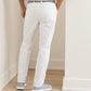 A person wearing Peter Millar’s eb66 Performance Five-Pocket Pant in white, paired with a light-colored shirt and gray sneakers, stands with hands in pockets facing a light-colored wall and floor.