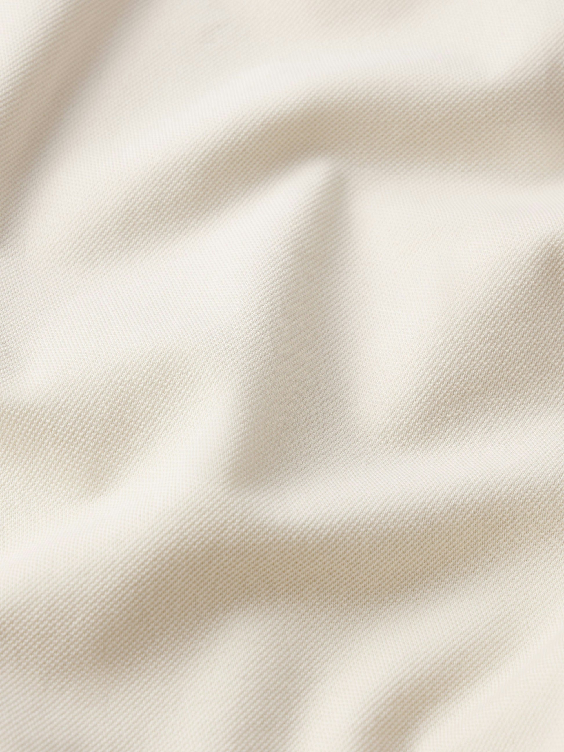 Close-up of FRAME's Light Pique Polo in cream-colored cotton piqué, showcasing its textured weave and soft folds—a timeless essential for everyday style.