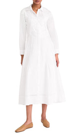 A person wearing a white Merlette Liberty Dress by Merlette New York with a collar and buttons down the front, paired with brown slip-on shoes, embodies sustainable fashion.