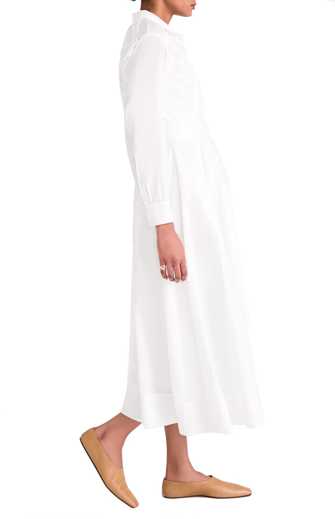 Side view of a person wearing a long white Merlette New York Merlette Liberty Dress and tan loafers, standing against a plain white background.