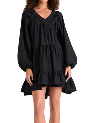 A person wearing a black Merlette New York Merlette Dawn Dress with balloon sleeves and a tiered, ruffled design is shown from the hips up.