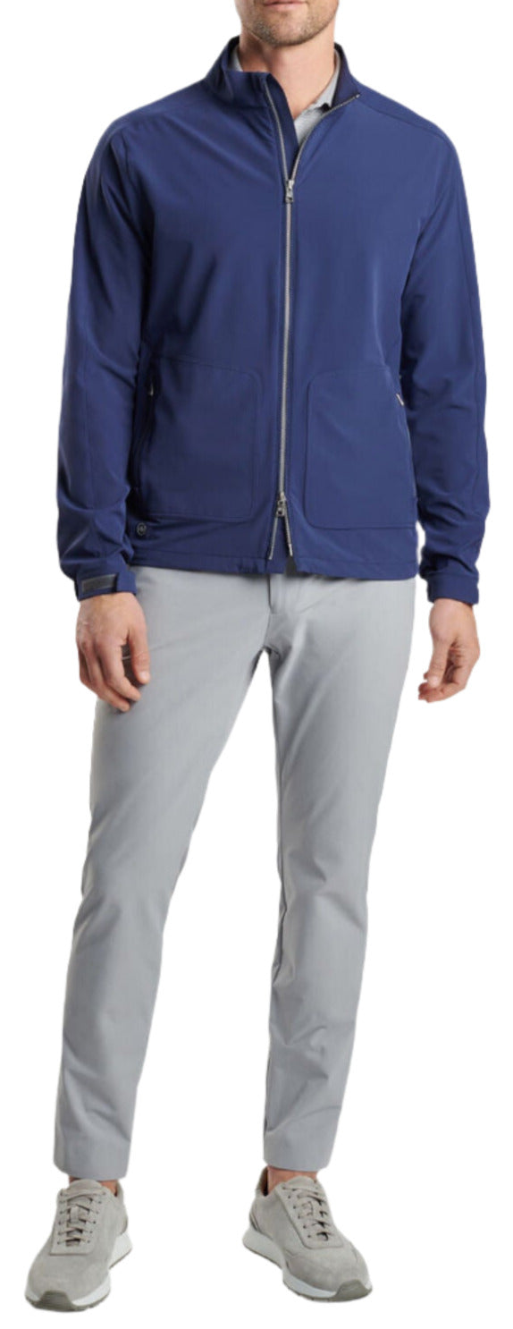 A person is wearing a Peter Millar Contour Jacket in blue, paired with light gray trousers and gray sneakers. The image is focused on the clothing.