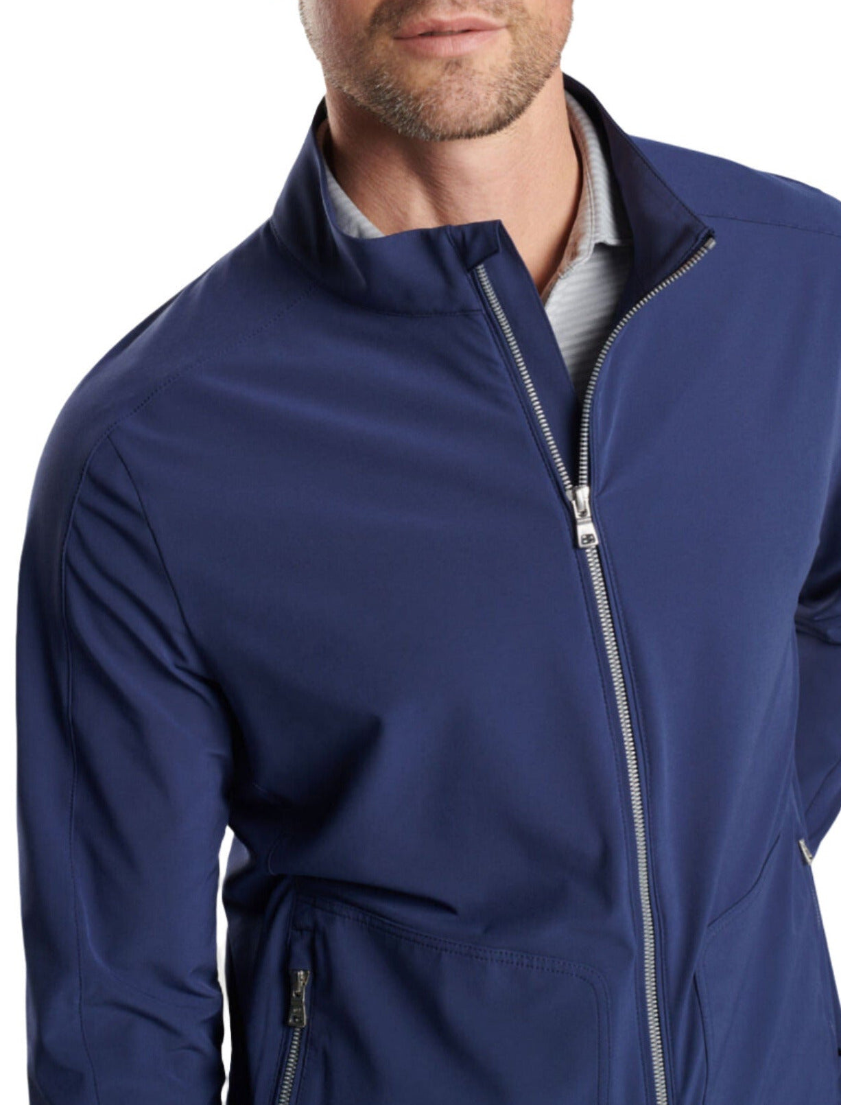 A man in a blue Peter Millar Contour Jacket with a stand collar, partially unzipped to reveal a grey shirt underneath. The man's face is partially visible, with short facial hair, and the jacket from Peter Millar boasts four-way stretch for added comfort.