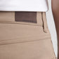Close-up of a person wearing Peter Millar eb66 Performance Five-Pocket Pants in tan, featuring a brown leather patch on the waistband. Made from stretch performance twill for extra comfort.