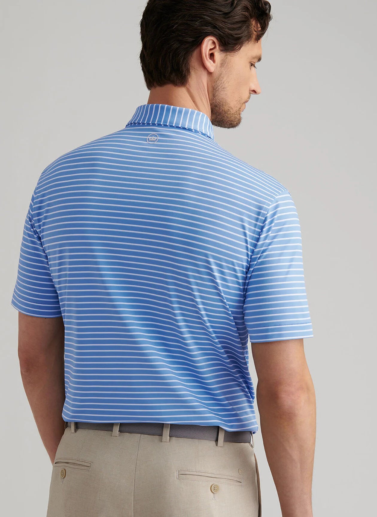 A man shown from the back wears a Peter Millar Dunnes Performance Jersey Polo in light blue and white stripes with UPF 50+ protection, paired with beige pants.