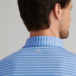 A man with short brown hair is shown from behind wearing a blue and white striped Peter Millar Dunnes Performance Jersey Polo, featuring a small round logo on the upper back, UPF 50+ sun protection, and four-way stretch for comfort.