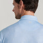 A man with short brown hair is seen from behind, wearing a light blue patterned Peter Millar Oyster Shooter Performance Jersey Polo with UPF 50+ protection, and looking to his left.
