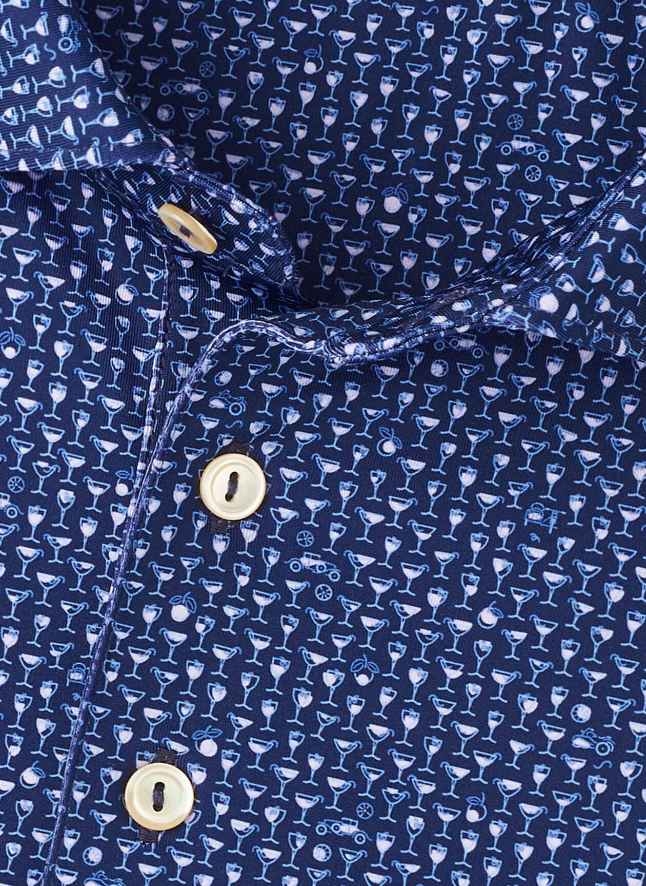Close-up of the Peter Millar Sidecar Performance Jersey Polo in blue, featuring a small white cocktail glass pattern, gold-colored buttons, and four-way stretch fabric for maximum comfort.