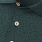 Close-up of a green Peter Millar No Slow Play Performance Jersey Polo featuring a subtle dark abstract pattern, four beige buttons on the placket, and four-way stretch for enhanced comfort.