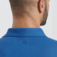 A man shown from behind wears the Peter Millar Lyons Performance Jersey Long-Sleeve Polo in blue, featuring a small circular crown logo below the collar and UPF 50+ sun protection for comfort outdoors.