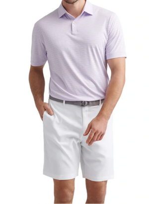A man wearing the Peter Millar Featherweight Payne Stripe Performance Polo, a gray belt, and white shorts stands with one hand in his pocket against a plain background.