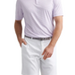 A man wearing the Peter Millar Orange Crush Performance Jersey Polo with four-way stretch and UPF 50+, paired with white shorts and a gray belt, stands with one hand in his pocket against a white background.