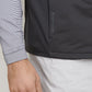 A person wearing a dark Peter Millar Fuse Hybrid Vest, a striped shirt, and white pants.