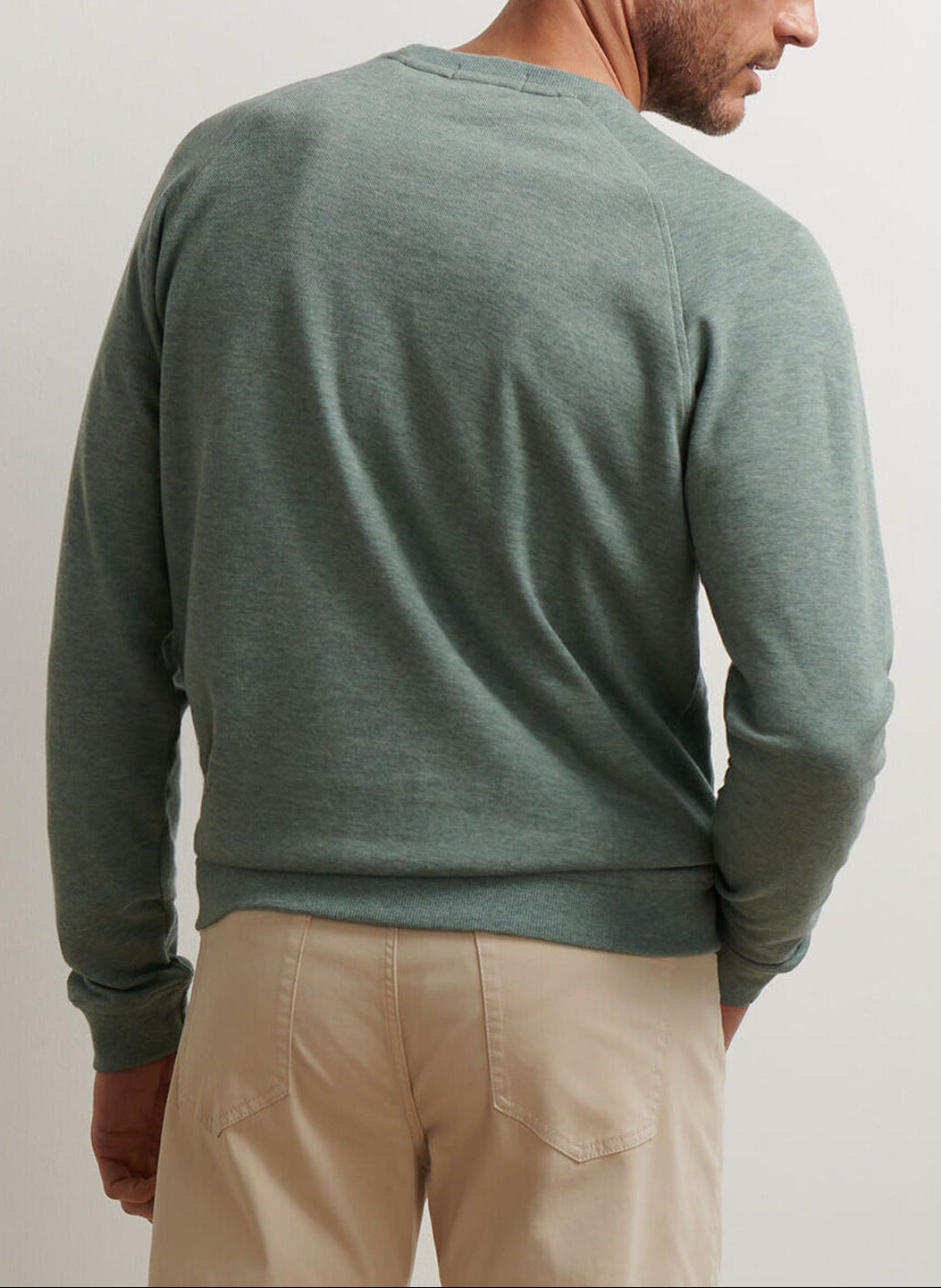A man is shown from the back wearing the Peter Millar Crown Comfort Knit Crew in light green and beige pants against a plain background.