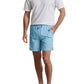A man stands with one hand in his pocket against a white background, wearing a white polo shirt, light blue Peter Millar Tropics Swim Trunk, and gray sneakers.