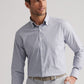 A man wears the Peter Millar Cashiers Performance Twill Sport Shirt in light blue and white checks with light gray pants, standing with one hand in his pocket and looking to the side.
