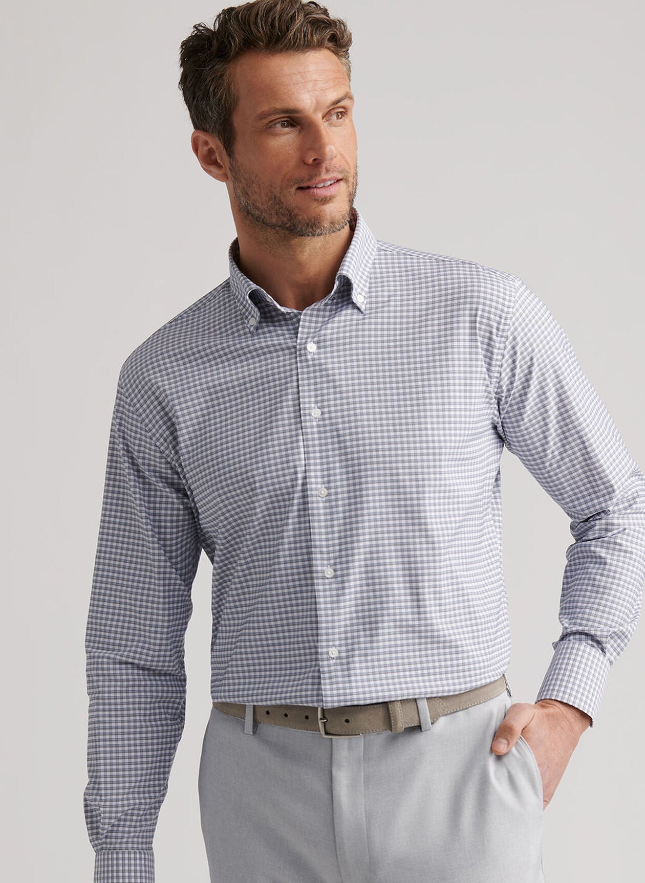 A man wears the Peter Millar Cashiers Performance Twill Sport Shirt in light blue and white checks with light gray pants, standing with one hand in his pocket and looking to the side.