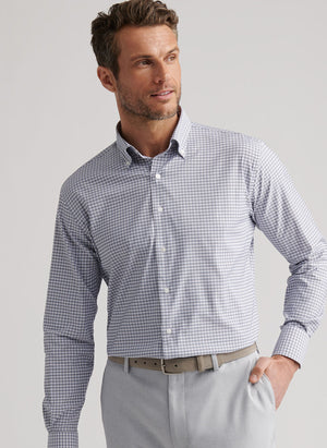 A man wears the Peter Millar Cashiers Performance Twill Sport Shirt in light blue and white checks with light gray pants, standing with one hand in his pocket and looking to the side.