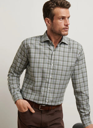 A man wears the Peter Millar Whitecap Performance Flannel Sport Shirt, a long-sleeve green and gray plaid shirt made from lightweight performance fibers, as he looks to his right against a plain background.