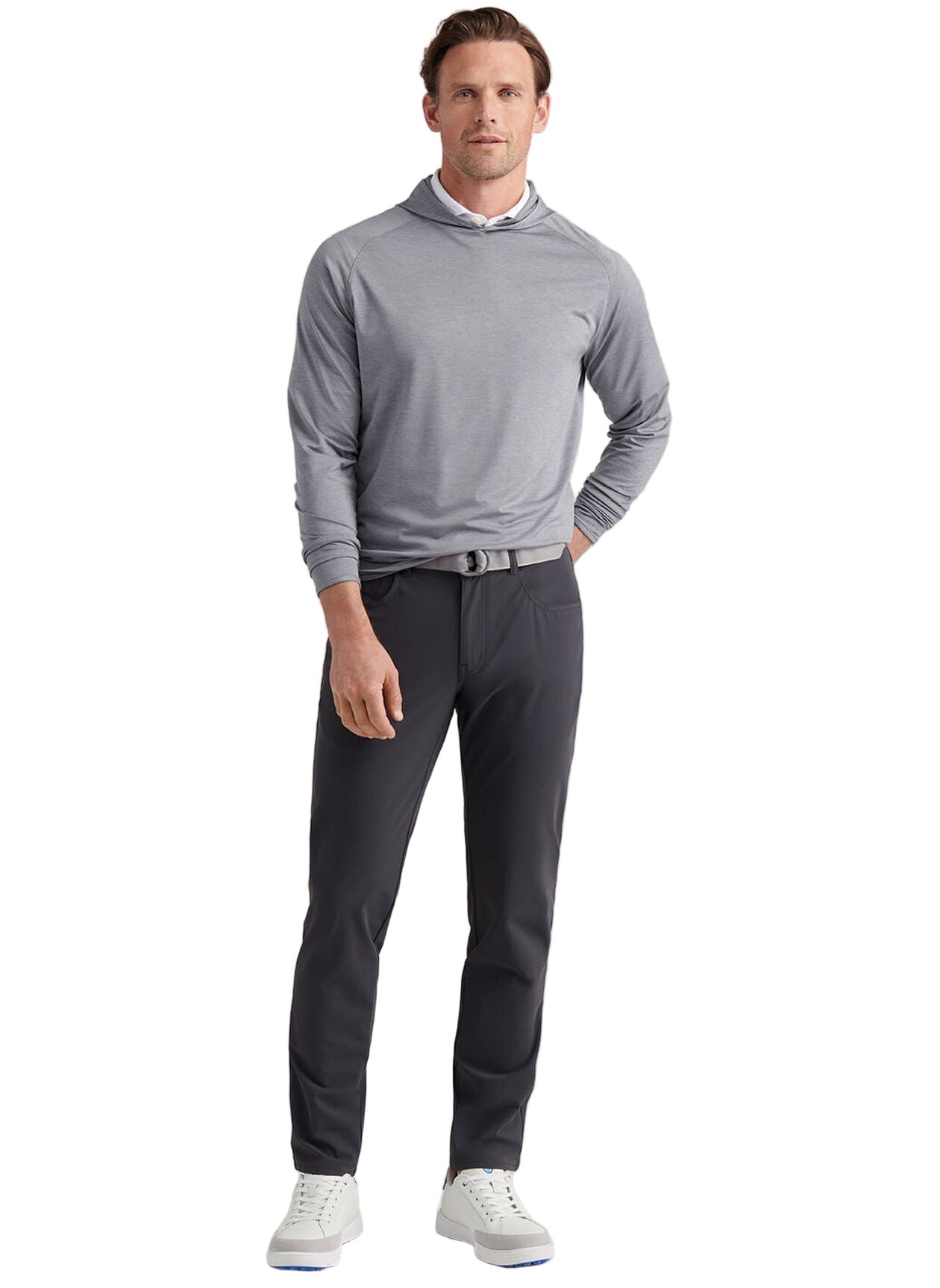 A man faces forward against a plain white background wearing Peter Millar Bingham Performance Five-Pocket Pant in dark gray, a light gray hooded long-sleeve shirt, and white sneakers.