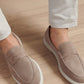 A person wearing Peter Millar Excursionist Penny Loafers, featuring water-resistant suede and lightweight EVA outsoles, pairs them with light-colored pants while standing on a light wooden floor.