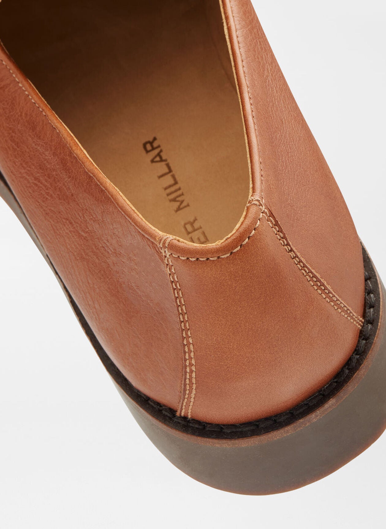 Close-up of the Madison Penny Loafer by Peter Millar, crafted from tumbled calf leather with detailed stitching, a thick sole, and "PETER MILLAR" printed on the insole.