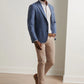 A man stands indoors wearing the Peter Millar Delrose Plaid Soft Jacket, a white dress shirt, beige trousers, and brown shoes on a light wood floor.
