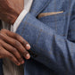 Someone adjusts their Delrose Plaid Soft Jacket by Peter Millar—blue plaid Italian fabric—styled over a light check shirt. A beige handkerchief adds a refined touch, making this jacket a versatile wardrobe essential.