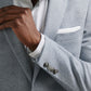 A man adjusts the lapel of the Peter Millar Barclay Knit Soft Jacket in light grey, featuring a white pocket square and worn over a white striped dress shirt.