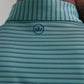 Close-up of the back of a person's neck wearing the Peter Millar Bridge Performance Jersey Polo—green and blue stripes, small blue crown logo below the collar, and UPF 50+ sun protection for comfort.