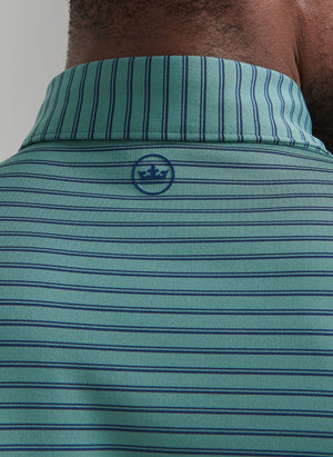Close-up of the back of a person's neck wearing the Peter Millar Bridge Performance Jersey Polo—green and blue stripes, small blue crown logo below the collar, and UPF 50+ sun protection for comfort.